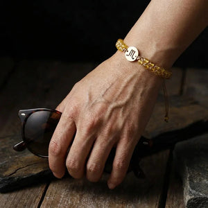 Yellow citrine Scorpio zodiac bracelet worn on a man's wrist holding sunglasses, gold sign charm on top