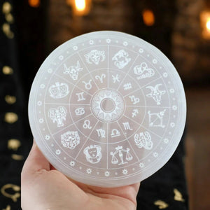 Translucent selenite recharging plate with engraved zodiac wheel held in hand