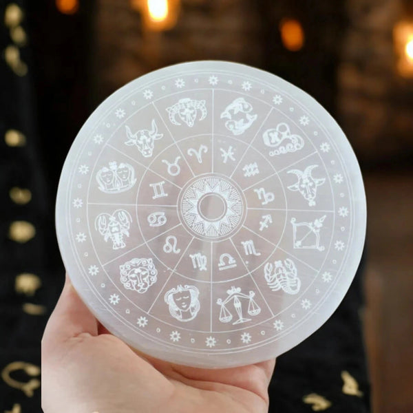 Translucent selenite recharging plate with engraved zodiac wheel held in hand