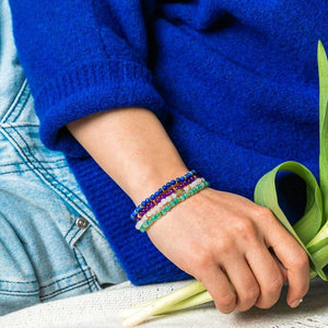 Close wrist view of four fine Soultheory Luck gemstone bracelets worn with a blue sleeve