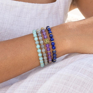 Close wrist view of four Soultheory Manifestation gemstone bracelets with the Soultheory charm